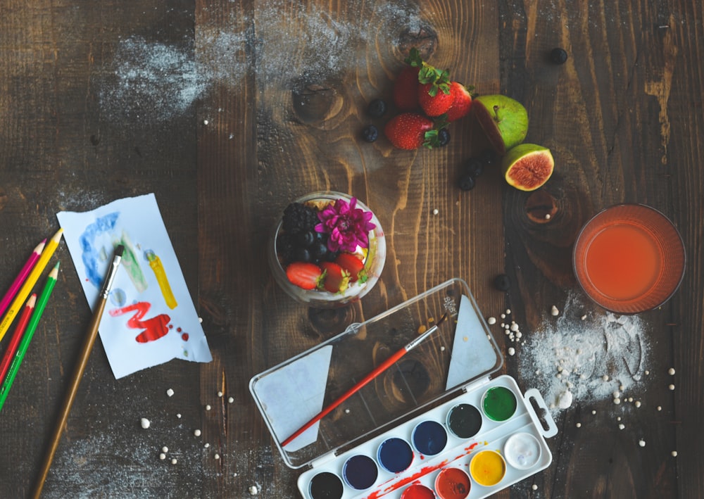 a wooden table topped with a bowl of fruit and paint