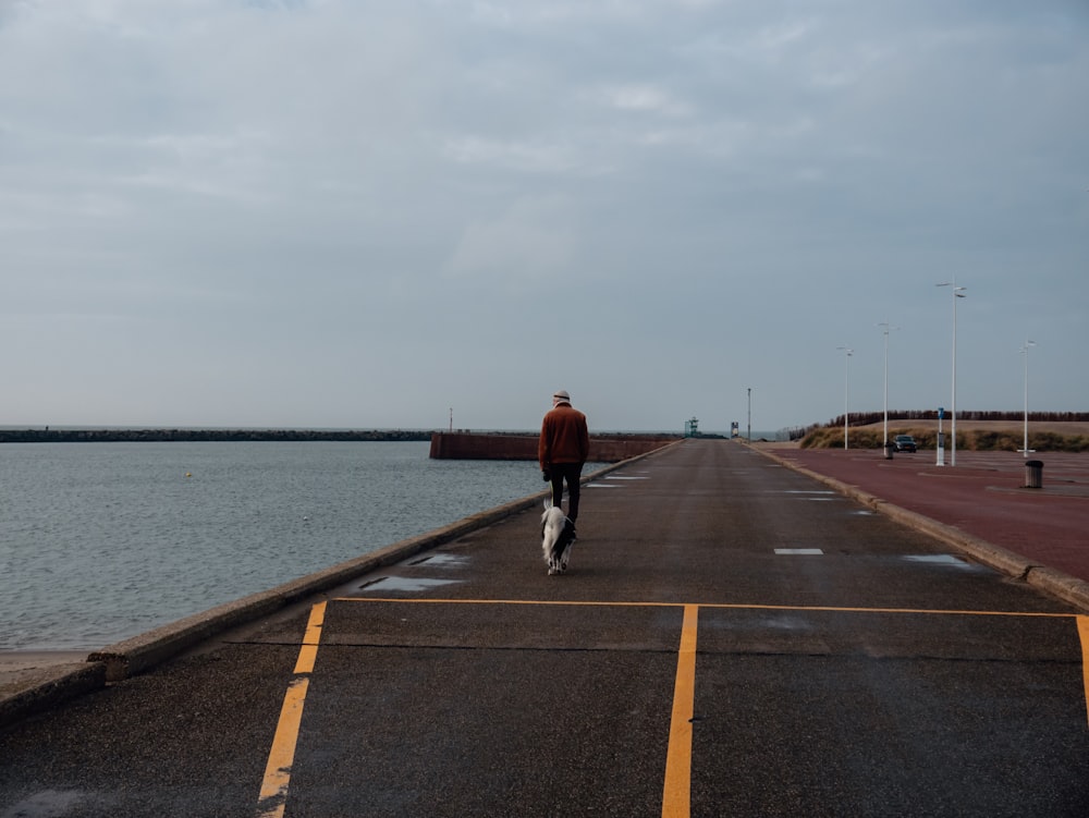 a man walking down a road next to a body of water