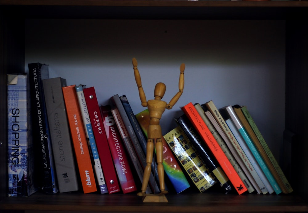 a wooden mannequin standing on top of a bookshelf