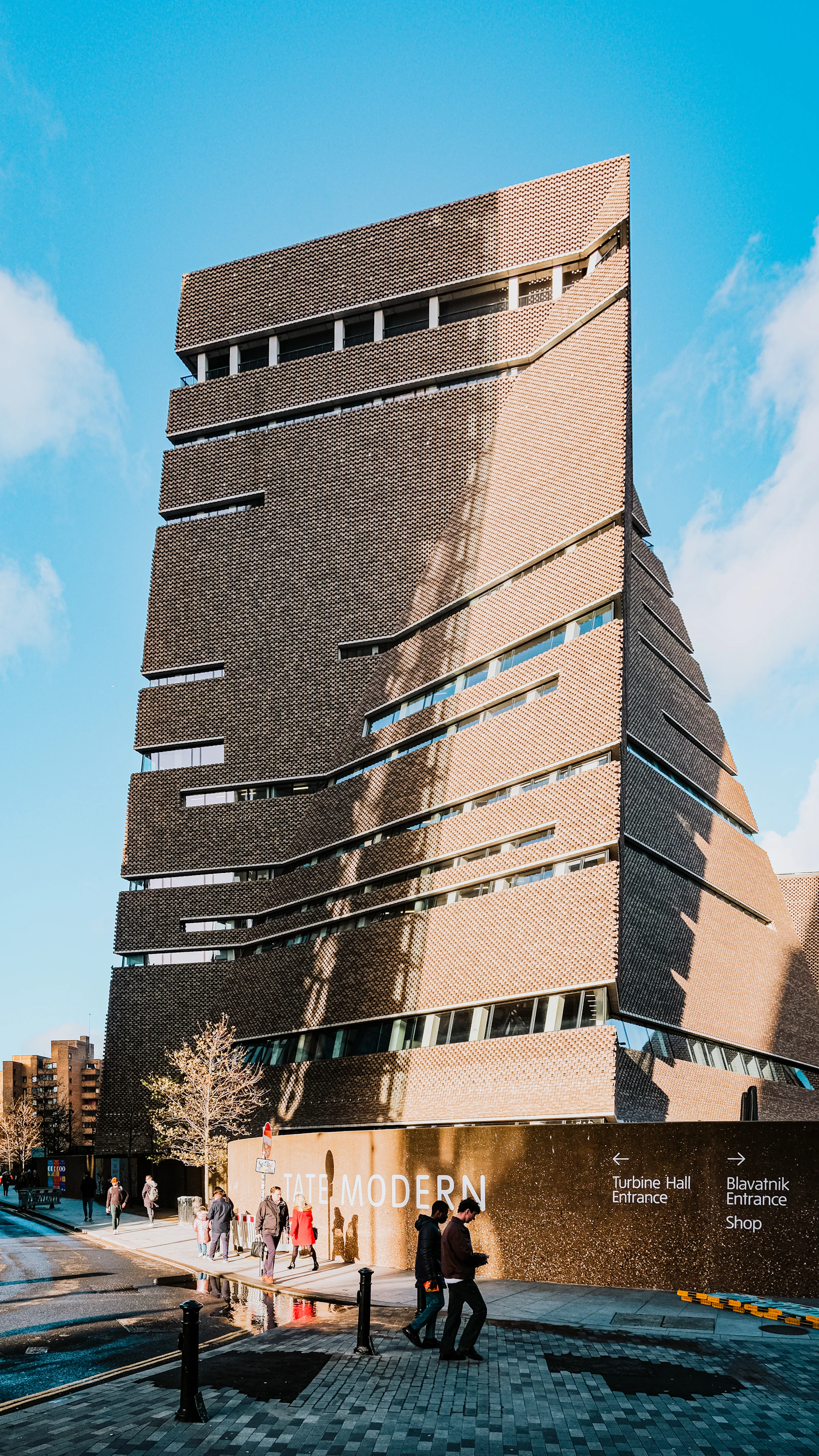 Travel photograph: People walking beside the brick tower and signed entrance of Tate Modern.