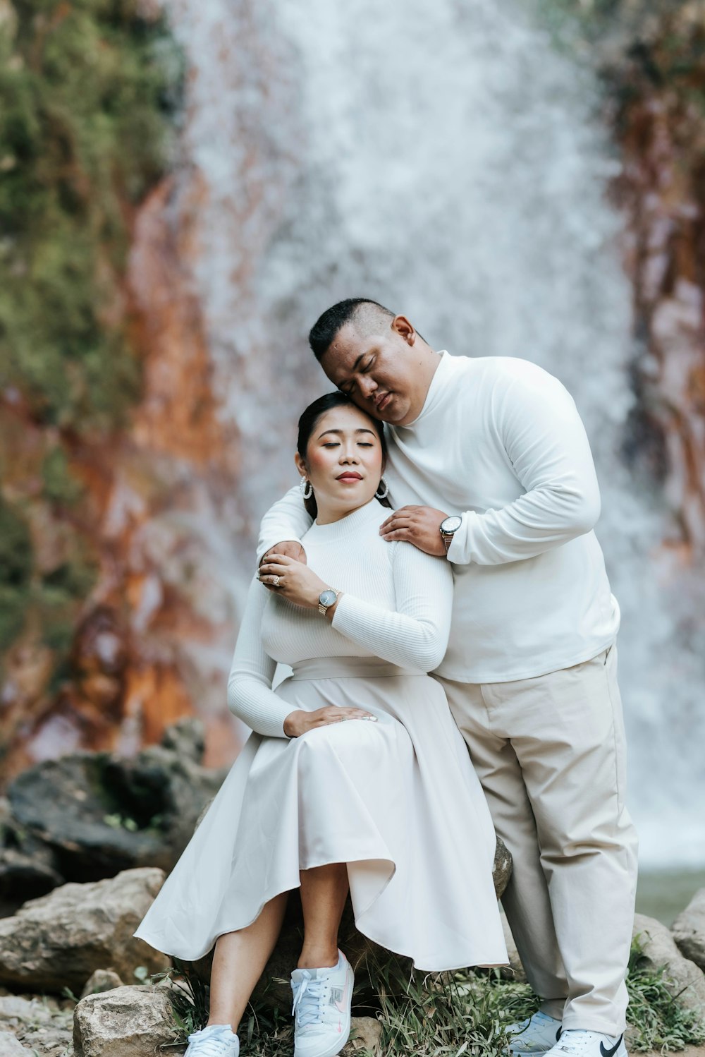 a man and a woman standing in front of a waterfall