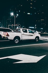 Modern tow truck with orange details parked on a lit urban street at night.
