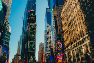 Tall buildings adorned with colorful advertisements and digital screens, bathed in warm sunlight. The iconic urban setting features bustling skyscrapers and vibrant displays.