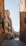 Narrow Venetian street lined with traditional, colorful buildings flanking a serene canal. Iron railings and a small pedestrian bridge in the distance enhance the charm of the scene. The buildings reflect warm, earthy tones under a clear blue sky.