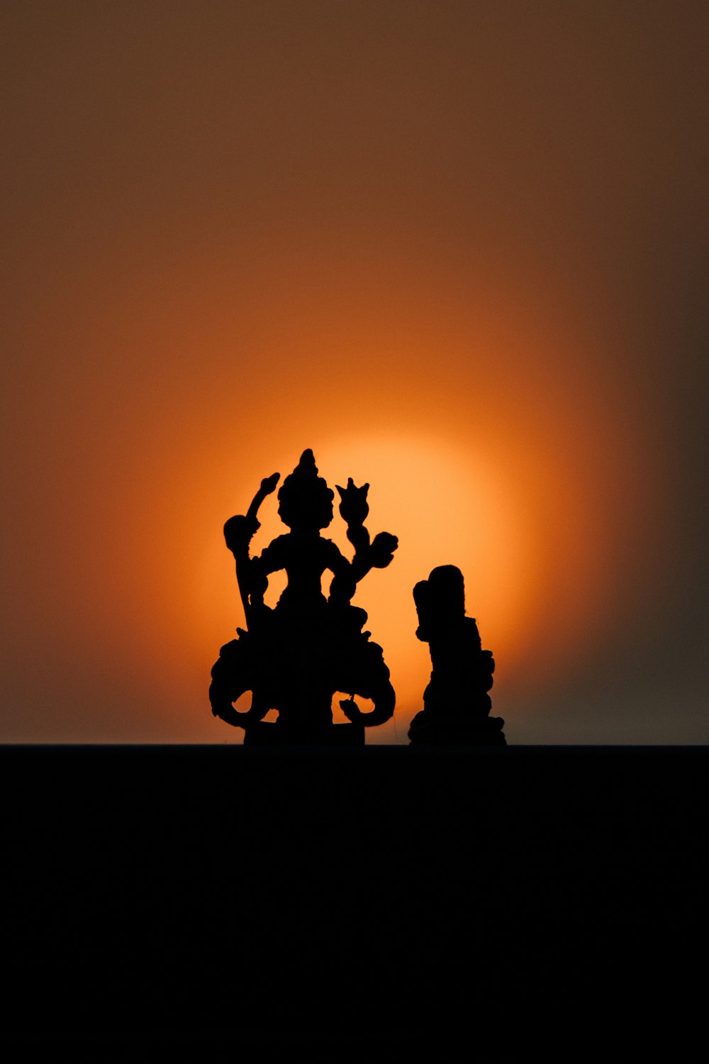 the sun is setting behind a silhouette of a statue