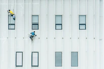 Close-up of a worker painting a building exterior at height with safety gear.