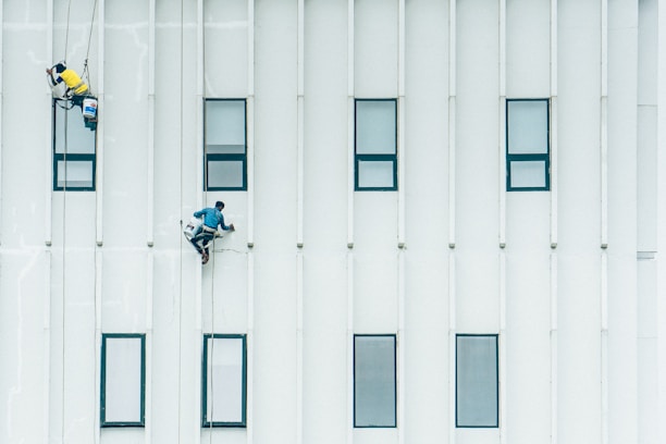 Technicians performing high-rise building painting with safety harnesses.
