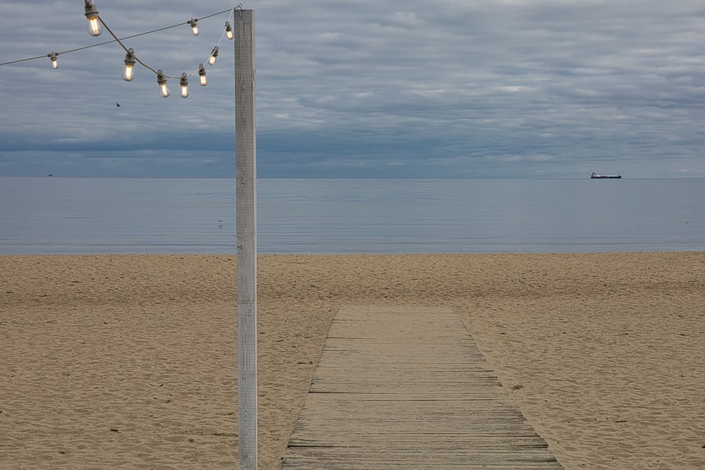 a wooden path leading to a beach with lights strung from it