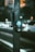 A pedestrian button is installed on a metal pole, which is located next to a road with blurred traffic in the background. The button is designed to prompt a change in the traffic signal for pedestrians. The scene takes place during nighttime, as indicated by the artificial lighting and soft bokeh effect created by car headlights.