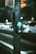 A pedestrian button is installed on a metal pole, which is located next to a road with blurred traffic in the background. The button is designed to prompt a change in the traffic signal for pedestrians. The scene takes place during nighttime, as indicated by the artificial lighting and soft bokeh effect created by car headlights.