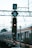 A commuter train is stationed or moving slowly on the tracks next to a signal post with a red light. The background features a lattice of overhead power lines and supports.