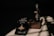 A bottle of perfume labeled 'CHIVAAS' sits on a textured rectangular block, accompanied by a promotional piece of paper with the phrase 'The True Magic of Perfume'. The scene is bathed in dramatic lighting creating strong shadows on the surface.