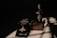 A bottle of perfume labeled 'CHIVAAS' sits on a textured rectangular block, accompanied by a promotional piece of paper with the phrase 'The True Magic of Perfume'. The scene is bathed in dramatic lighting creating strong shadows on the surface.