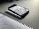 A notebook with handwritten notes in blue ink lies open on a dark tabletop. Beside it is a white pen and a smartphone with a case, showing a reflection of clouds on its screen.