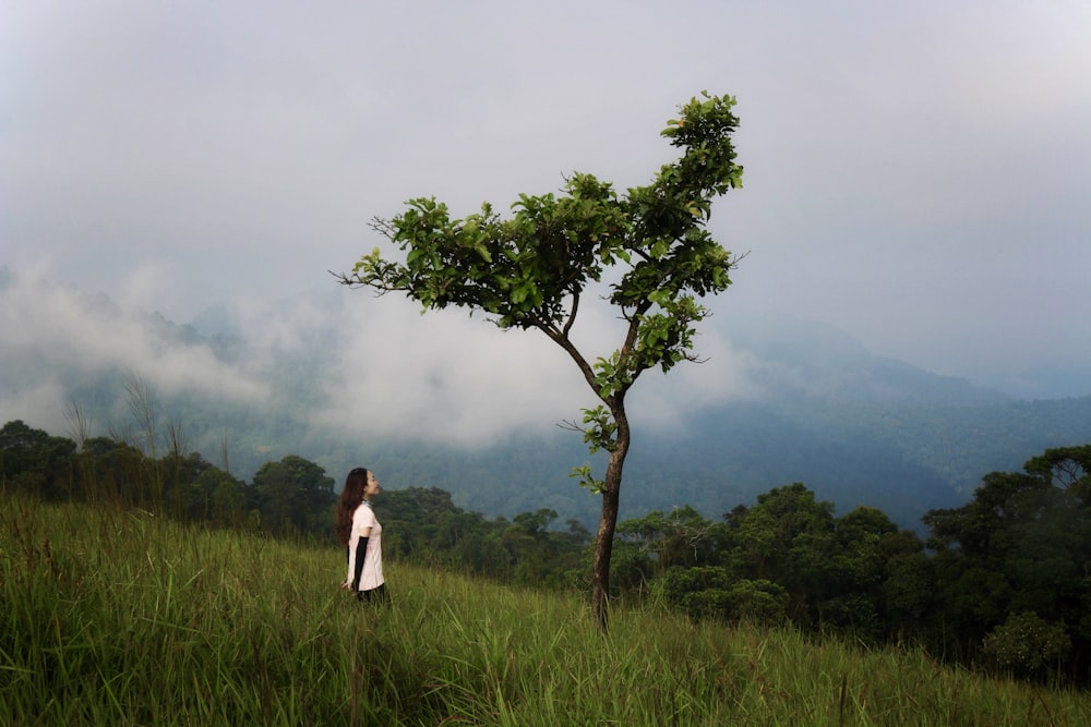 a woman standing in a field next to a tree