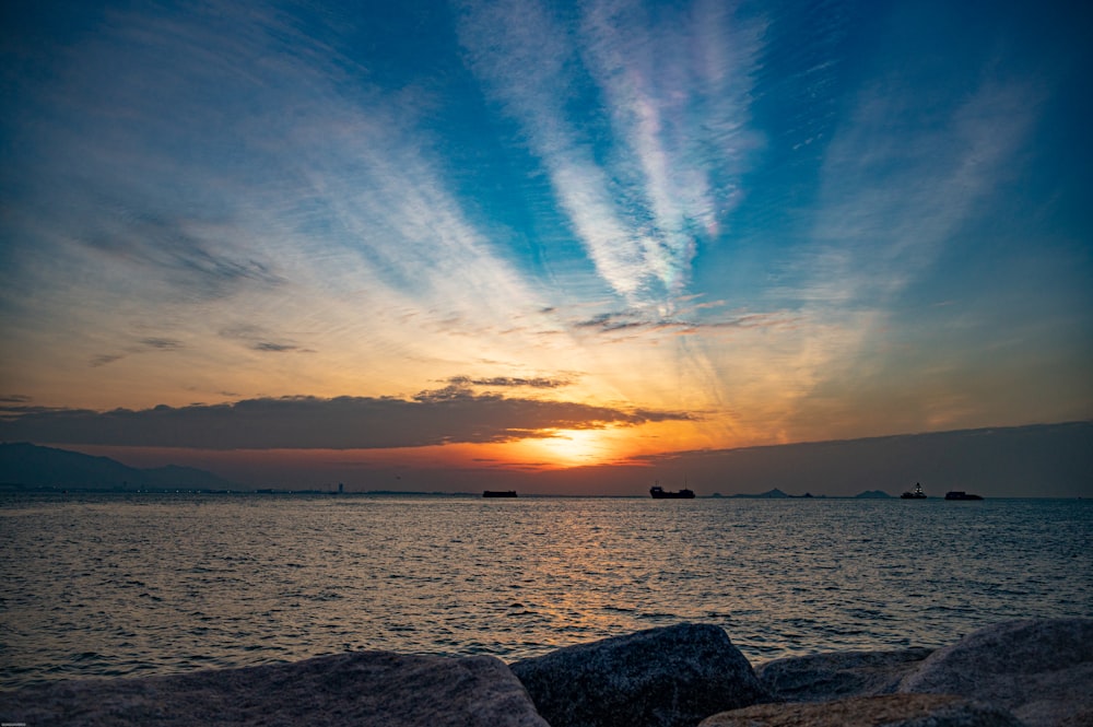 a sunset over a body of water with rocks in the foreground