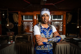 Stylish man wearing a black and gold kurta with festive embroidery, smiling warmly in a minimalist luxurious setting.