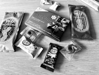 Various packaged snacks are arranged on a wooden surface, including Pocky sticks and multiple KitKat bars. The snacks have Japanese labeling and come in distinctive wrappers featuring almonds, chocolate, and more.