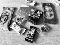 Various packaged snacks are arranged on a wooden surface, including Pocky sticks and multiple KitKat bars. The snacks have Japanese labeling and come in distinctive wrappers featuring almonds, chocolate, and more.