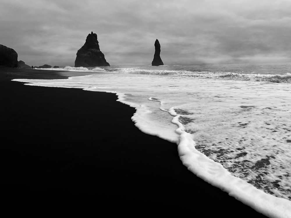 a black and white photo of a beach with a rock formation in the background