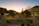 A scenic view of a university campus at sunset, featuring historical buildings, open walkways, and landscaped greenery. Street lights are illuminated as dusk sets in, with students or visitors walking and sitting on the steps in the foreground, observing the tranquil scene.