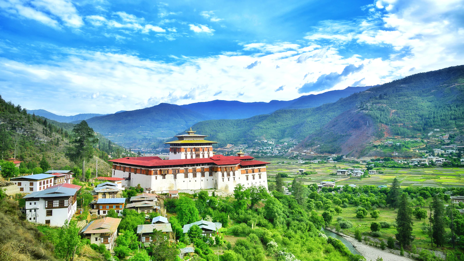 Rinpung Dzong on its hillside above the Paro valley in morning sun, green fields and farmhouses stretching away