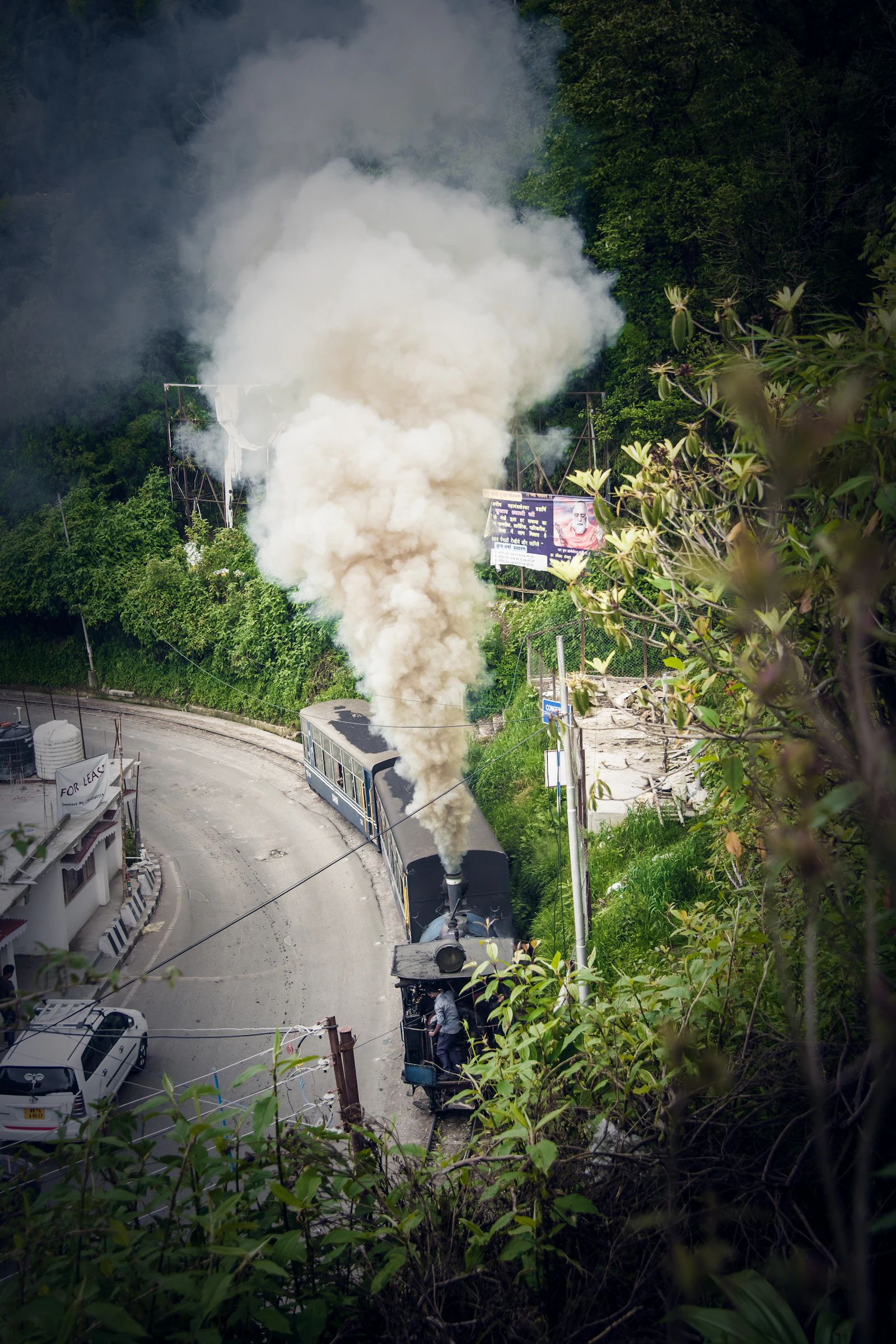 A Darjeeling toy train steam engine pouring white smoke as it rounds a bend of the road through Kurseong