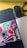 A workspace featuring a wireless keyboard, a mouse, and a pair of eyeglasses on a wooden surface. A laptop adorned with colorful stickers, including abstract designs and typography, adds a vibrant touch.