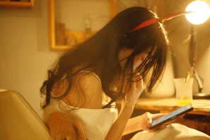 A candid shot of a woman smiling warmly while reading an eBook on a sleek tablet in a softly lit room.