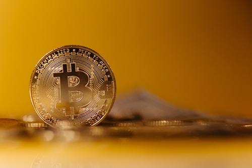 A close-up of a physical Bitcoin coin with intricate detailing, placed against a blurred golden background, conveying a sense of depth and focus on the cryptocurrency.