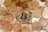 A large assortment of coins is scattered over paper currency, with a prominent Bitcoin coin at the center symbolizing cryptocurrency.