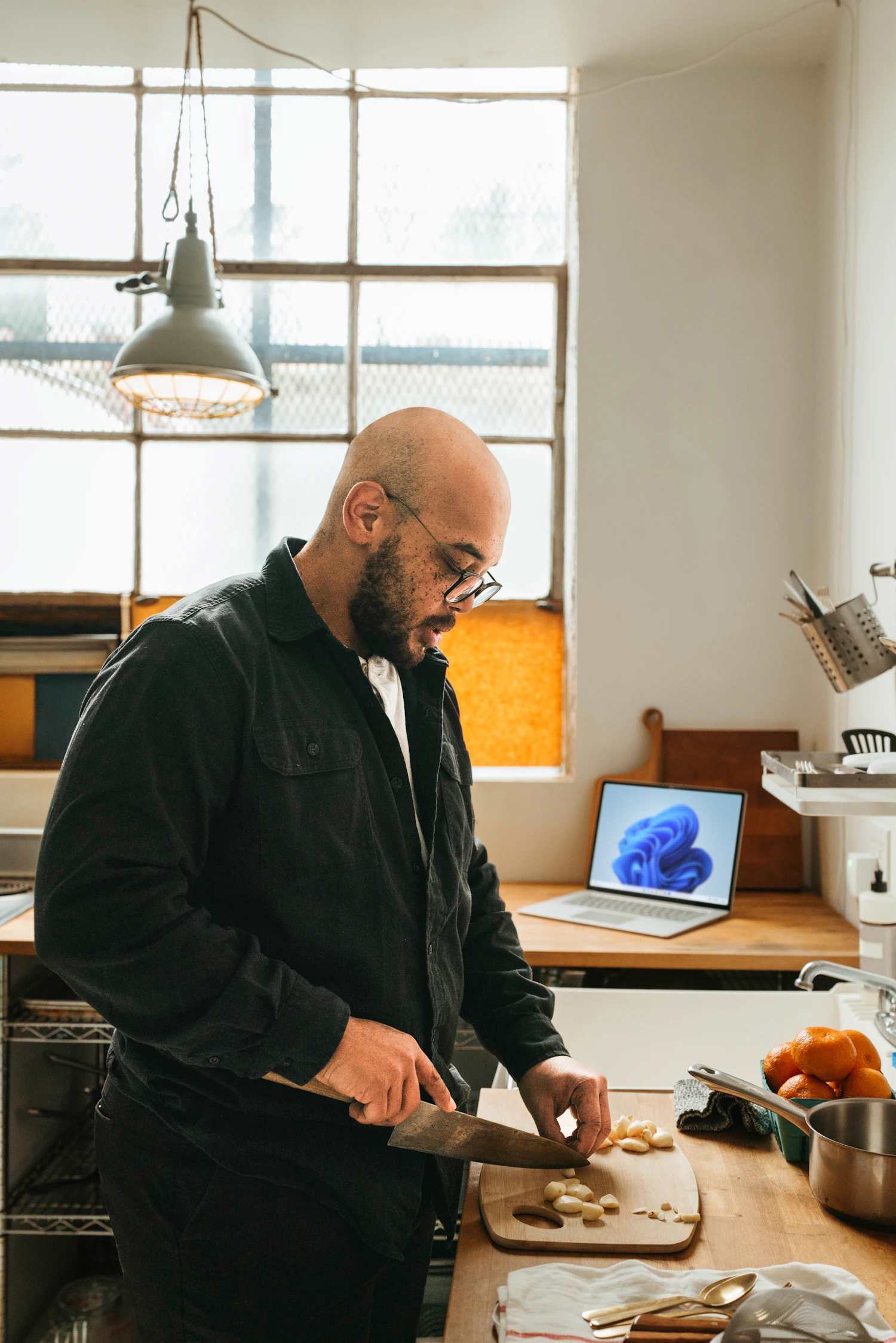 A bearded man chopping fruit at a table beside a window