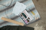 A scene with a tablet displaying interior design content, placed on a striped rug alongside design sketches, a screwdriver, wooden planks, and a rolled mat.