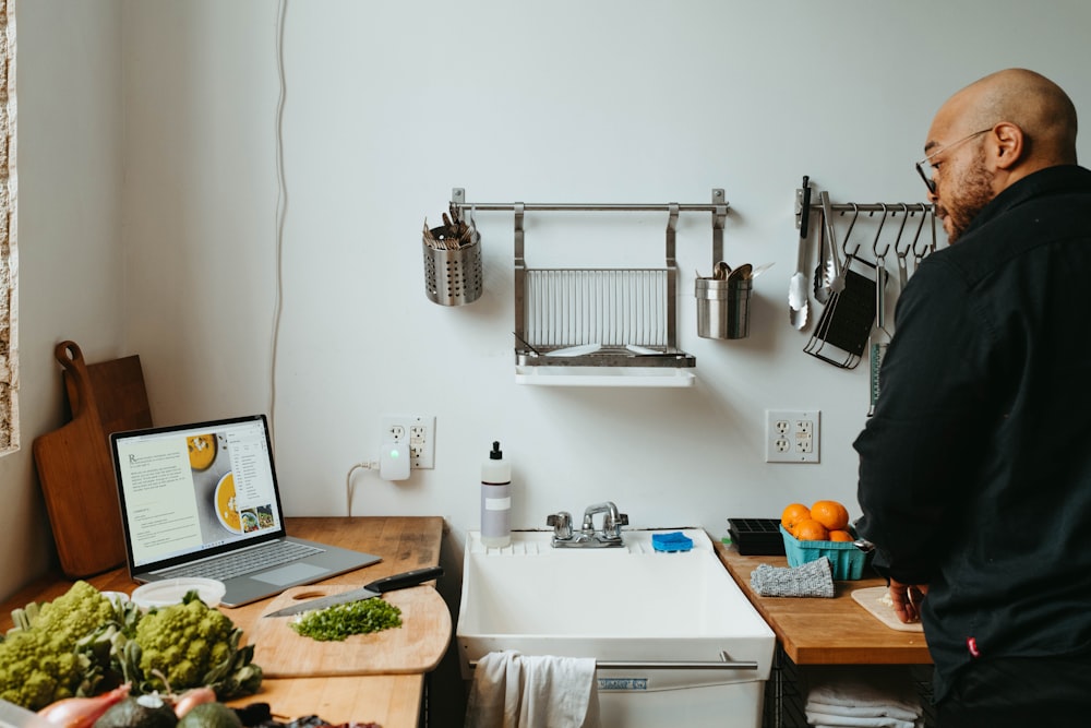 a man standing in a kitchen next to a laptop computer