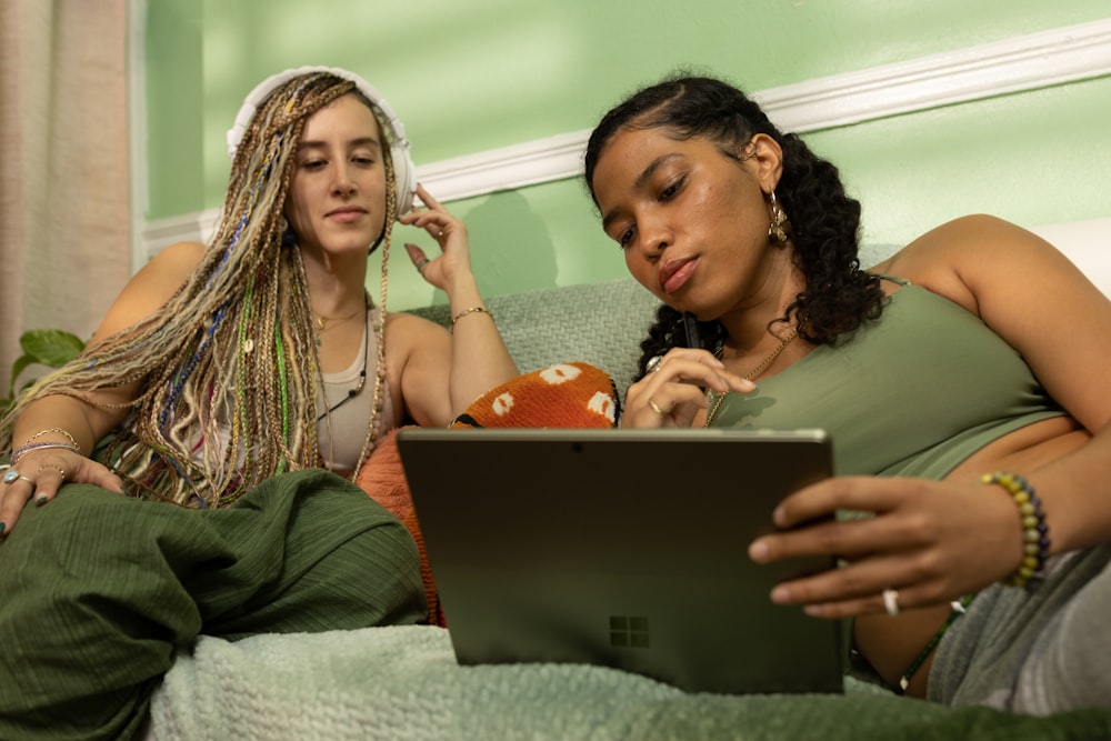 two women sitting on a bed looking at a laptop