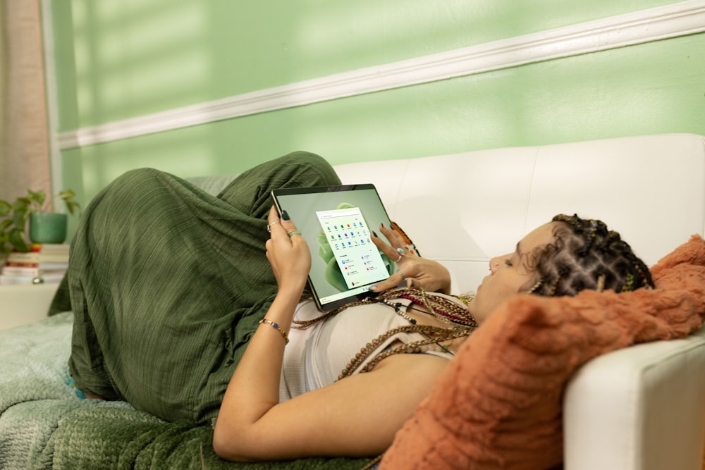a woman laying on a couch holding a tablet