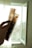 A hand is holding up two strips of photographic film negatives against a softly lit background with an open window. The film features multiple frames and is translucent, allowing light to pass through, revealing some details of the images captured on it.