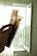 A hand is holding up two strips of photographic film negatives against a softly lit background with an open window. The film features multiple frames and is translucent, allowing light to pass through, revealing some details of the images captured on it.