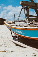 a blue and orange boat sitting on top of a sandy beach