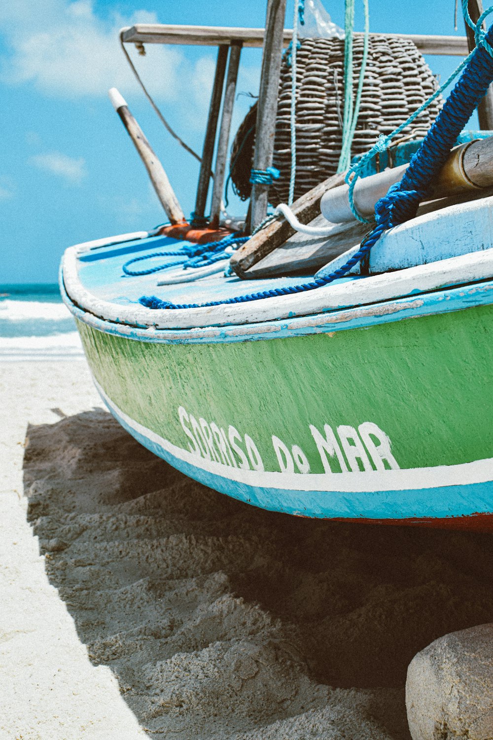 a green and blue boat sitting on top of a sandy beach