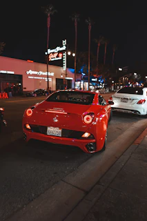 A shiny cherry-red compact car parked on a bustling city street at sunset