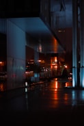 A cinematic still showing a dramatic urban night scene with deep shadows and vibrant red highlights.