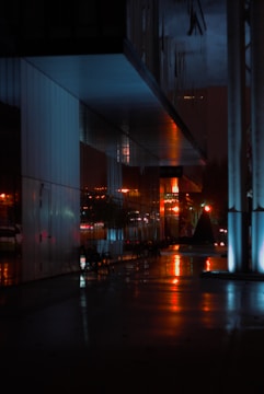 A cinematic still showing a dramatic urban night scene with deep shadows and vibrant red highlights.