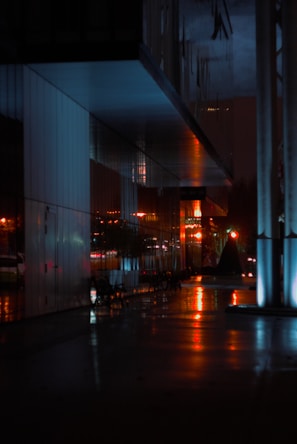 A sleek urban nightscape with smooth glass reflections and red accents.