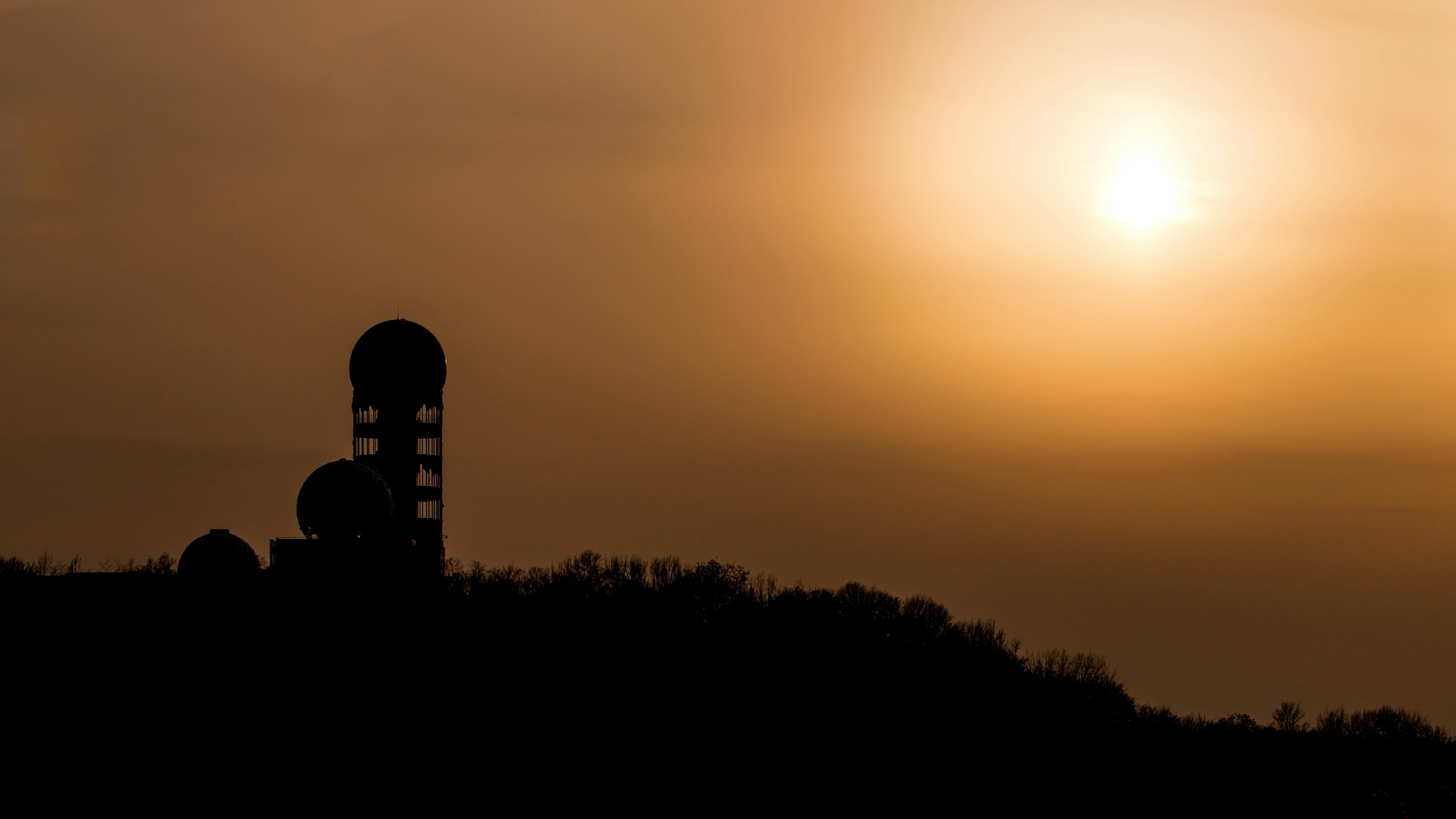 the sun is setting behind a tower on a hill