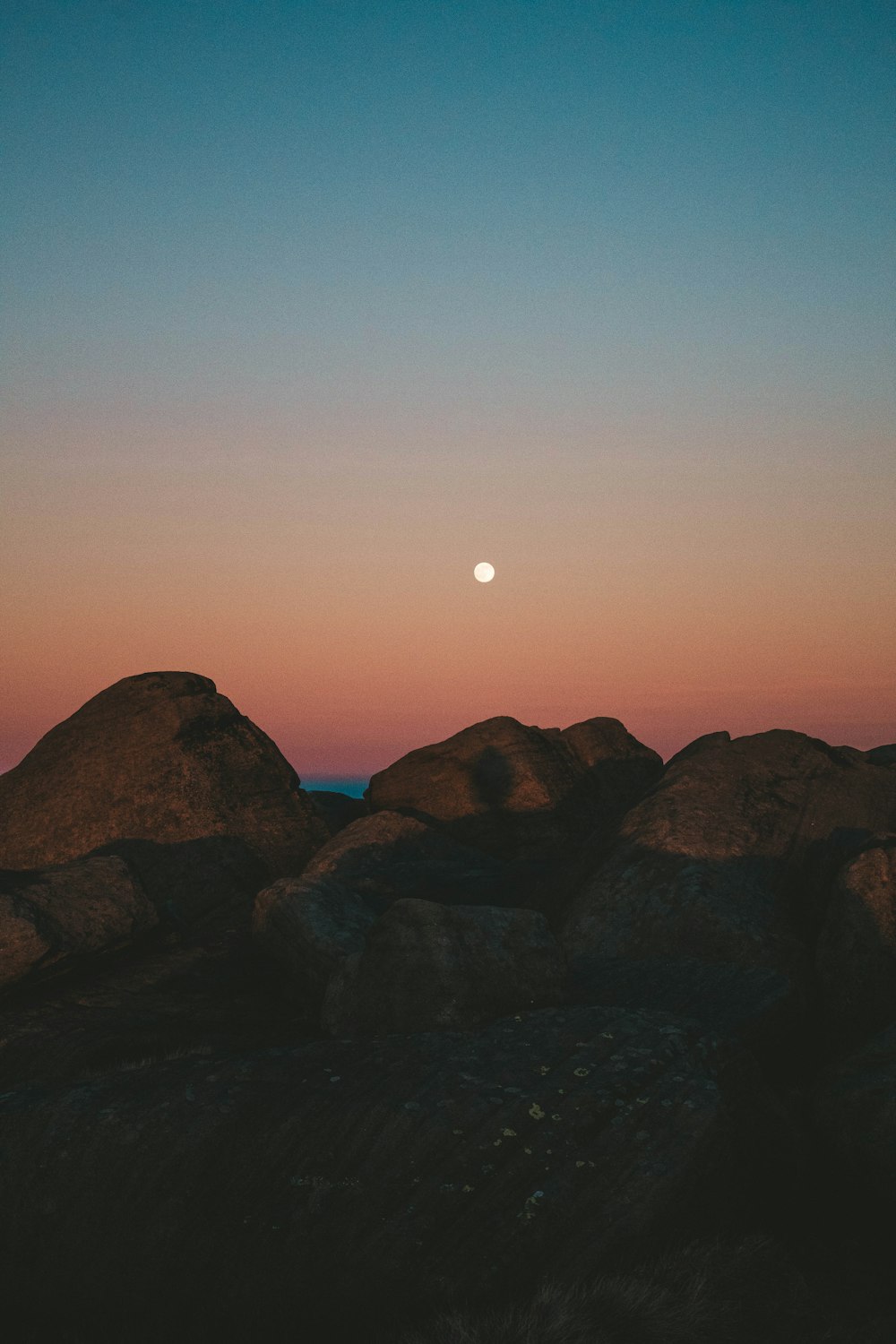 a full moon is seen over some rocks