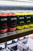 Rows of canned beverages displayed on a shelf, featuring branding that includes the words 'Drippy' and 'cannabis infused'. The cans are predominantly in red and yellow colors with black and white text. The background includes blurred shelves and packaging.