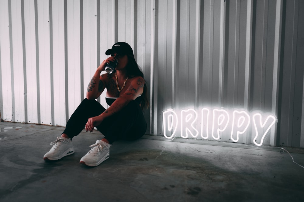 a man sitting on the ground next to a neon sign