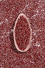A large collection of red beans spread across a surface with a pink, elongated dish at the center filled with more beans.
