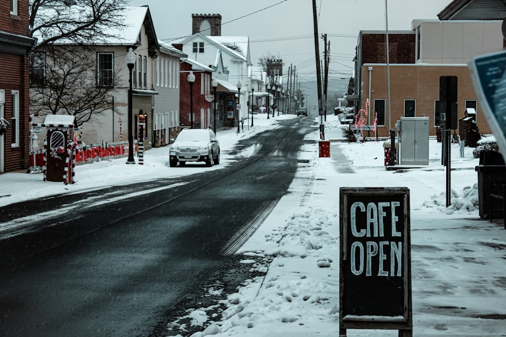 a snowy street with a sign that says cafe open